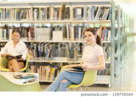 Female student reading book on chair in library 139758584