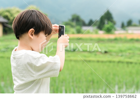 A boy taking pictures of rural scenery with his smartphone, a child's profile. A boy taking pictures of rural scenery with his smartphone, a child's profile. 139758662