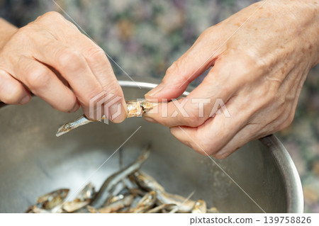 Senior woman removes the heads from dried sardines Senior woman removes the heads from dried sardines 139758826