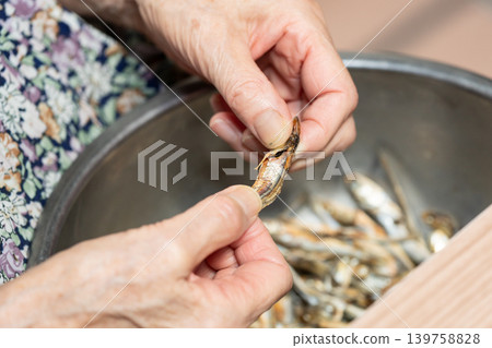 Senior woman removes the heads from dried sardines Senior woman removes the heads from dried sardines 139758828