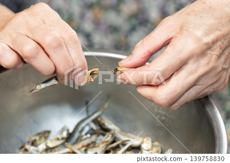 Senior woman removes the heads from dried sardines Senior woman removes the heads from dried sardines 139758830