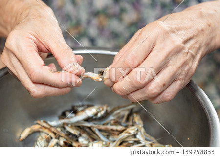 Senior woman removes the heads from dried sardines Senior woman removes the heads from dried sardines 139758833