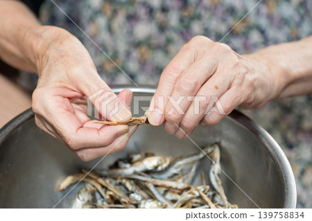 Senior woman removes the heads from dried sardines Senior woman removes the heads from dried sardines 139758834