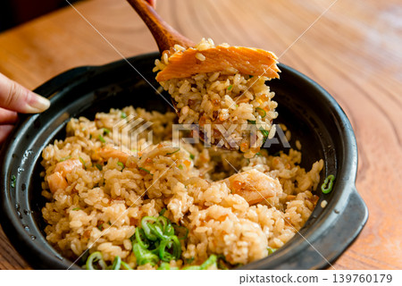 用木匙舀起陶罐裡煮好的鮭魚和鮭魚籽飯的場景。 用木匙舀起陶罐裡煮好的鮭魚和鮭魚籽飯的場景。 139760179