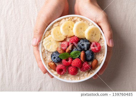 Healthy oatmeal breakfast bowl with raspberry, blueberry, banana and almond holding by woman hand 139760485