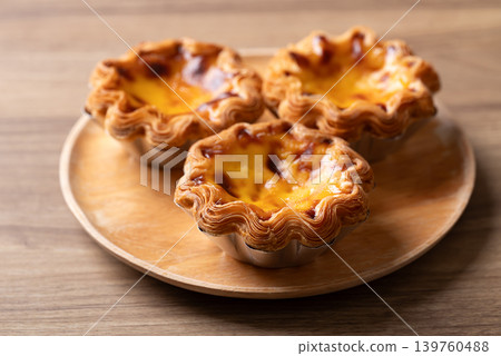 Egg tarts filled with creamy custard and caramelized tops on a wooden plate 139760488