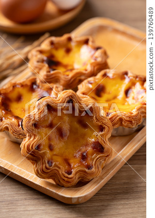 Egg tarts filled with creamy custard and caramelized tops on a wooden plate Egg tarts filled with creamy custard and caramelized tops on a wooden plate 139760489