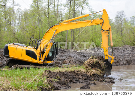Excavator picks up big amount of soil for construction irrigation system canal in countryside for watering Excavator picks up big amount of soil for construction irrigation system canal in countryside for watering 139760579