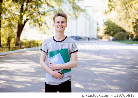 Cheerful young student with folder and exercise books enjoying walk in the park near university in the evening after classes Cheerful young student with folder and exercise books enjoying walk in the park near university in the evening after classes 139760612