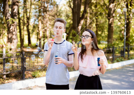 Boyfriend and girlfriend blowing soap bubbles in park in the evening, having fun together Boyfriend and girlfriend blowing soap bubbles in park in the evening, having fun together 139760613