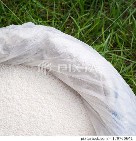 Plastic bag of white mineral fertilizer against a green lawn in a sunny day. 139760641