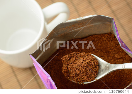 Spoon with some ground coffee against a big pack of coffee near the empty cup. Making coffee in the morning Spoon with some ground coffee against a big pack of coffee near the empty cup. Making coffee in the morning 139760644
