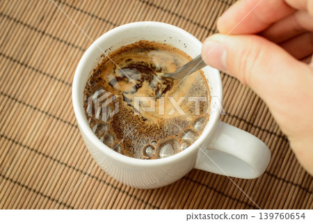 Man`s hand stirs coffee with a spoon. Making coffee in the morning. Man`s hand stirs coffee with a spoon. Making coffee in the morning. 139760654
