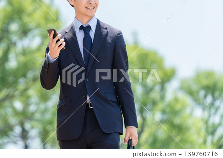 一位男性商務人士手持智慧型手機,在戶外行走。 一位男性商務人士手持智慧型手機,在戶外行走。 139760716