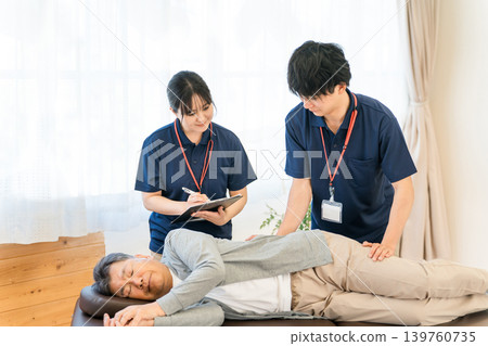 一位老年男子在復健期間接受按摩和伸展運動,以及包括物理治療師和職業治療師在內的男性工作人員 一位老年男子在復健期間接受按摩和伸展運動,以及包括物理治療師和職業治療師在內的男性工作人員 139760735