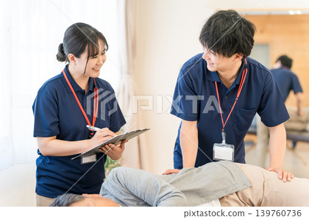 一位老年男子在復健期間接受按摩和伸展運動,以及包括物理治療師和職業治療師在內的男性工作人員 一位老年男子在復健期間接受按摩和伸展運動,以及包括物理治療師和職業治療師在內的男性工作人員 139760736