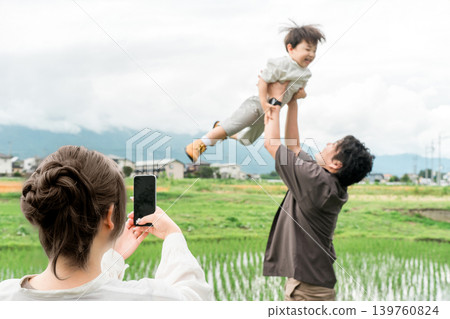 A dad lifting his child up high, a mom taking pictures of the family with her smartphone. 139760824