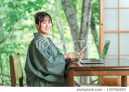 A woman in a yukata working on her laptop and smartphone in a room at a hot spring inn. A woman in a yukata working on her laptop and smartphone in a room at a hot spring inn. 139760885