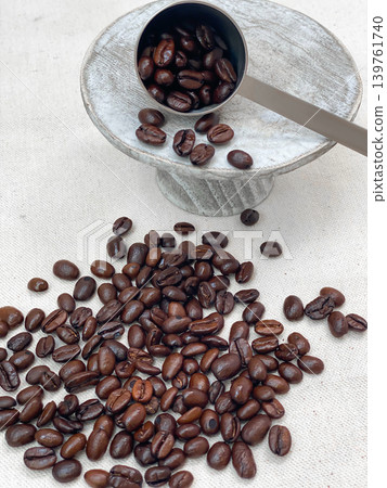 A measuring spoon and scattered roasted coffee beans on a wooden stand. A measuring spoon and scattered roasted coffee beans on a wooden stand. 139761740