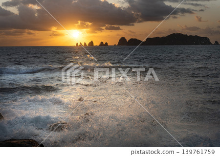 A view of the sunrise over the Nanatsu-iwa rocks off the coast of Hyuga-nada Sea and the crashing waves from Inozakibana Park Campground in Nichinan City, Miyazaki Prefecture. A view of the sunrise over the Nanatsu-iwa rocks off the coast of Hyuga-nada Sea and the crashing waves from Inozakibana Park Campground in Nichinan City, Miyazaki Prefecture. 139761759