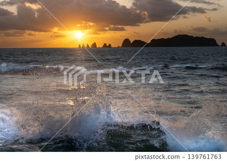 A view of the sunrise over the Nanatsu-iwa rocks off the coast of Hyuga-nada Sea and the crashing waves from Inozakibana Park Campground in Nichinan City, Miyazaki Prefecture. A view of the sunrise over the Nanatsu-iwa rocks off the coast of Hyuga-nada Sea and the crashing waves from Inozakibana Park Campground in Nichinan City, Miyazaki Prefecture. 139761763