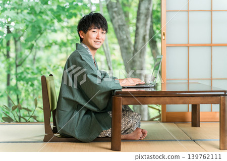 A man in a yukata working on a computer in a room at a hot spring inn A man in a yukata working on a computer in a room at a hot spring inn 139762111
