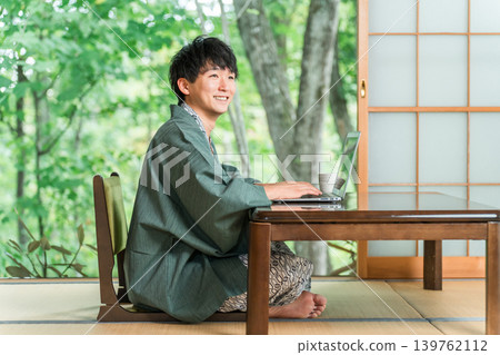 A man in a yukata working on a computer in a room at a hot spring inn A man in a yukata working on a computer in a room at a hot spring inn 139762112