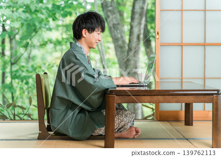 A man in a yukata working on a computer in a room at a hot spring inn 139762113