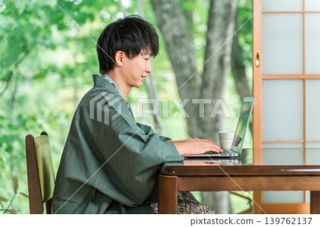A profile view of a man in a yukata working on his laptop in a room at a hot spring inn. A profile view of a man in a yukata working on his laptop in a room at a hot spring inn. 139762137