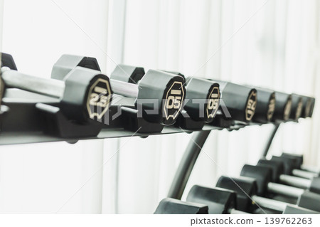 A row of black dumbbells on a storage rack in a fitness center. 139762263
