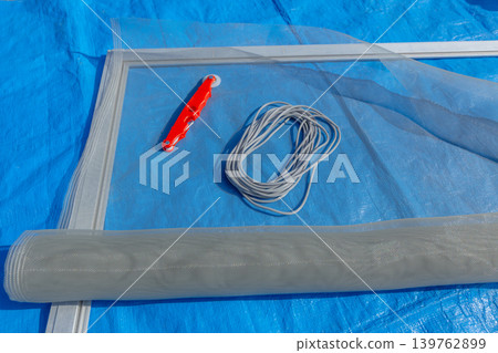 戶外更換紗門的準備場景：藍色防水布上擺放著DIY工具和紗窗。 139762899