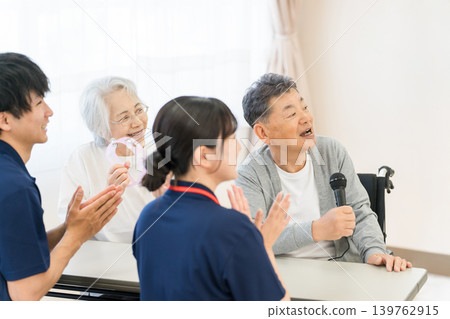 Elderly people and male and female caregivers singing karaoke in a group home or nursing home Elderly people and male and female caregivers singing karaoke in a group home or nursing home 139762915