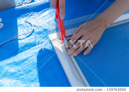 A woman's hands are seen replacing a screen door mesh outdoors, showing a DIY maintenance task. A woman's hands are seen replacing a screen door mesh outdoors, showing a DIY maintenance task. 139763000