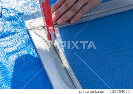A woman's hands are seen replacing a screen door mesh outdoors, showing a DIY maintenance task. 139763003