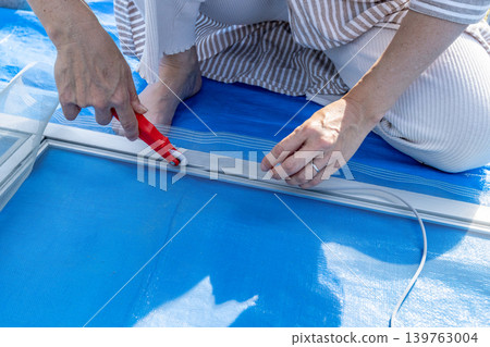 A woman's hands are seen replacing a screen door mesh outdoors, showing a DIY maintenance task. 139763004