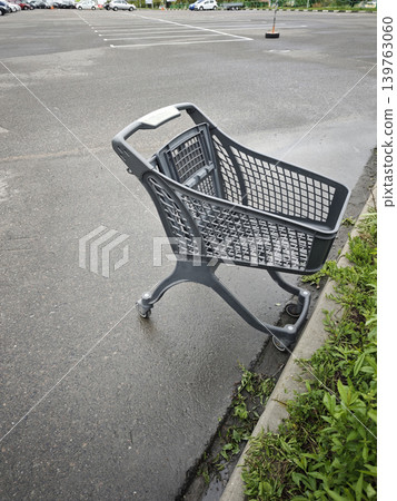 Abandoned grey shopping cart left alone on wet asphalt in an empty parking Abandoned grey shopping cart left alone on wet asphalt in an empty parking 139763060