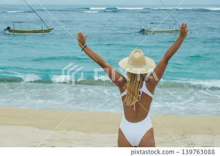 Woman stands on the beach with arms raised toward the ocean Woman stands on the beach with arms raised toward the ocean 139763088