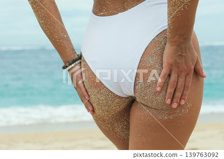 Woman with sandy skin stands by the ocean with hands on hips Woman with sandy skin stands by the ocean with hands on hips 139763092