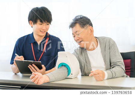 一位老人用血壓計測量血壓,一位護士做筆記,一位男性護理人員 一位老人用血壓計測量血壓,一位護士做筆記,一位男性護理人員 139763658