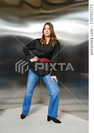 Woman poses in black shirt and blue jeans in modern studio with reflective background Woman poses in black shirt and blue jeans in modern studio with reflective background 139763773