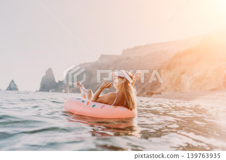 Woman beach ocean. Happy woman relaxing on inflatable donut ring in the sea with scenic cliffs. Woman beach ocean. Happy woman relaxing on inflatable donut ring in the sea with scenic cliffs. 139763935