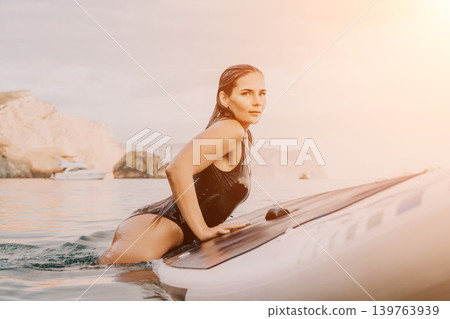 Woman Paddle Board Water Sports - A woman sits on a paddle board in the water, looking ahead. Woman Paddle Board Water Sports - A woman sits on a paddle board in the water, looking ahead. 139763939