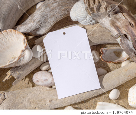 Blank vertical gift tag mockup on sand near seashells and driftwood with hard shadows, label design Blank vertical gift tag mockup on sand near seashells and driftwood with hard shadows, label design 139764074