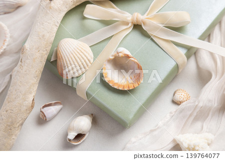 Sage green gift box with ribbon bow near seashells and driftwood top view. Coastal summer packaging Sage green gift box with ribbon bow near seashells and driftwood top view. Coastal summer packaging 139764077