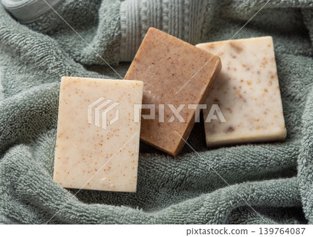 Brown and beige handmade solid soap bars on sage green bath towel. Exfoliating scrub soap set Brown and beige handmade solid soap bars on sage green bath towel. Exfoliating scrub soap set 139764087