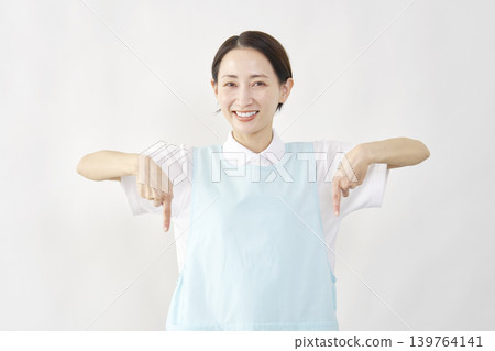 Female caregiver points downwards against a white background. 139764141