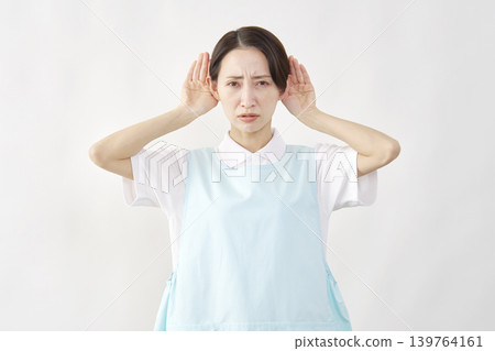 A female caregiver with her hand to her ear against a white background. A female caregiver with her hand to her ear against a white background. 139764161