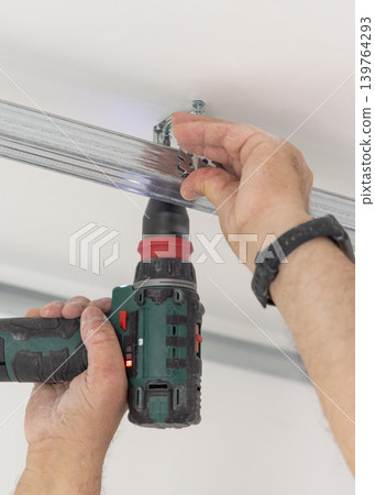 Construction worker using drill on metal frame for drywall suspended ceiling in apartment renovation Construction worker using drill on metal frame for drywall suspended ceiling in apartment renovation 139764293