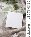 Christmas card mockup on wrapped sage green gift box with ribbon bow and fir branch, top view 139764310