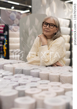 Senior woman browsing wallpaper rolls, planning home renovation and decor Senior woman browsing wallpaper rolls, planning home renovation and decor 139765443
